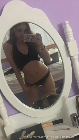 Woman in black lingerie posing in mirror selfie in bedroom.