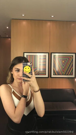 Woman in white and brown top taking mirror selfie in modern room with framed art.
