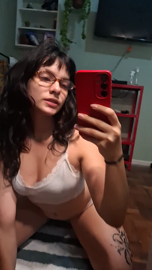 Dark-haired woman with glasses in white lingerie taking bedroom selfie.