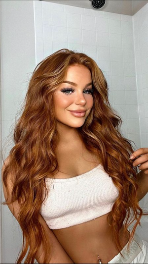 Woman with long wavy hair in white crop top, standing in tiled shower.