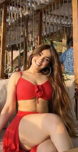 Woman in red bikini posing indoors, long hair, smiling, seated.