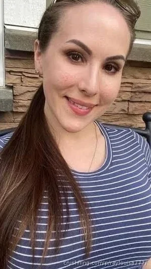 Woman with long brown hair in a striped shirt, smiling in front of a stone wall.