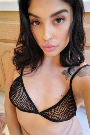 Woman with dark hair in mesh bra, bathroom selfie.