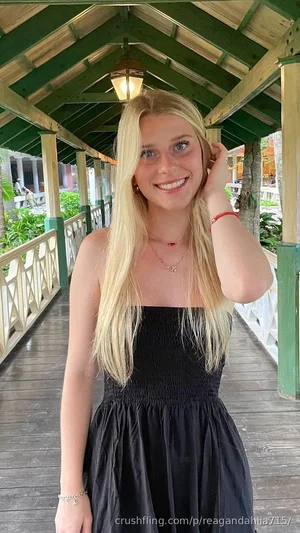 Blonde woman in black strapless dress smiling on covered wooden walkway.