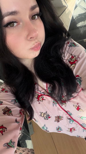 Woman with long dark hair in pink cat pajamas taking selfie indoors.