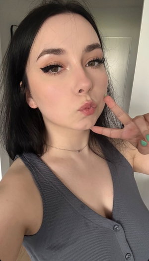 Woman with dark hair in gray top taking indoor selfie.