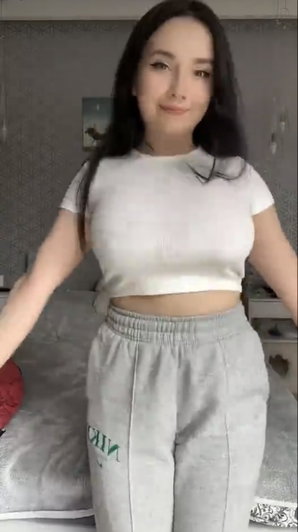 Asian woman in white crop top and grey sweatpants in bedroom.