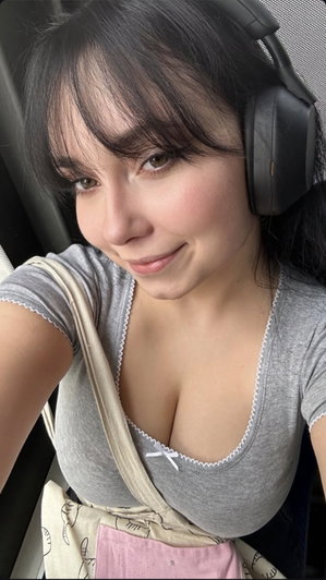 Woman with dark hair wearing gray top and headphones, sitting in a car.
