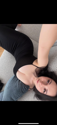 Woman in black bodysuit taking selfie on couch.