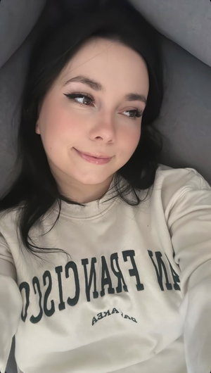 Woman with dark hair in sweatshirt taking selfie indoors.