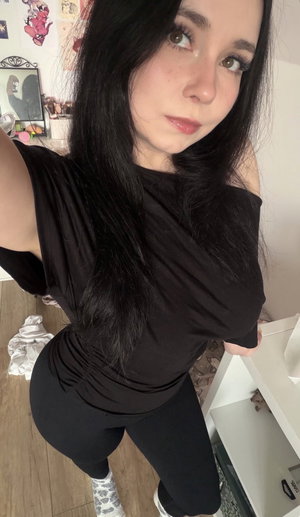 Woman with black hair in off-shoulder top and leggings in bedroom.