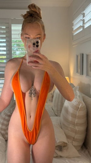 Woman in orange halter swimsuit taking mirror selfie in bedroom.
