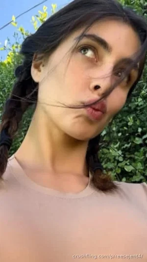 Woman with dark braided hair in a beige top, making a playful face outdoors.