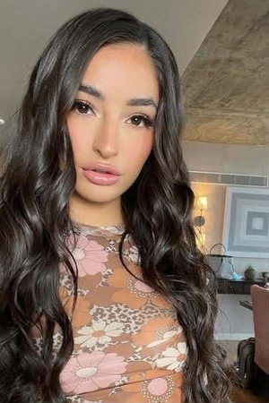 Woman with long dark hair wearing floral lace top indoors.