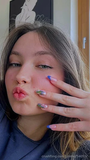 Woman with long brown hair and floral nail art making a playful face indoors.