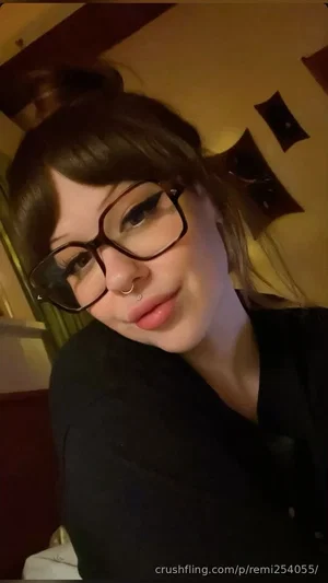 Woman with glasses and nose ring, wearing black top, in indoor setting.