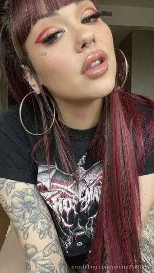 Woman with red hair, tattoos, and black graphic tee in indoor setting.