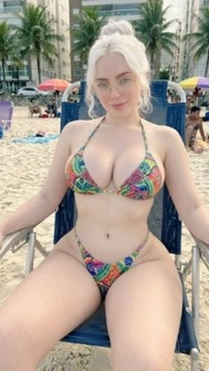 Woman with platinum hair in colorful bikini sitting on beach chair at sandy beach.