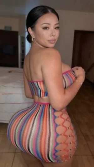 Woman in colorful striped dress posing in bedroom, back to camera.