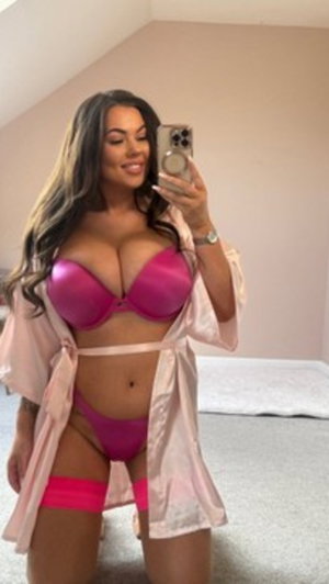 Woman in pink lingerie taking mirror selfie in bedroom.