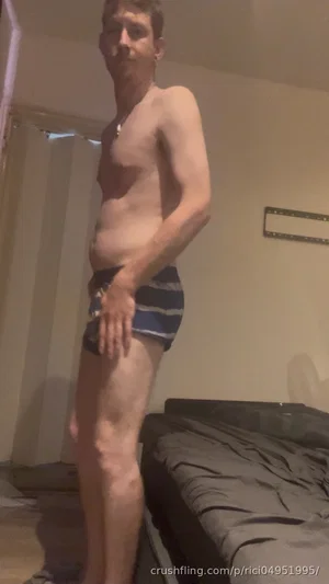 Man in striped underwear standing in a bedroom, bare-chested, hand on thigh.