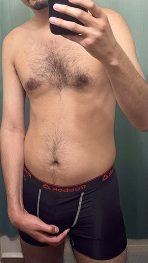 Shirtless man with hairy torso taking mirror selfie in black underwear.