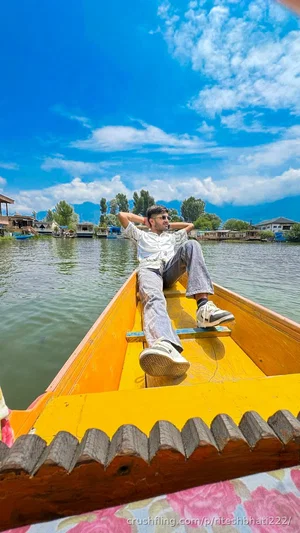 Man in white shirt and jeans sitting in a yellow boat on a lake with mountains in the background.