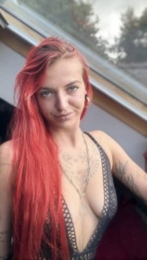 Red-haired woman in black lace top with tattoos.