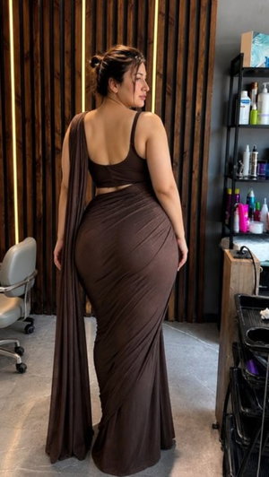 Woman in brown draped dress standing in salon, back view, hair in bun.