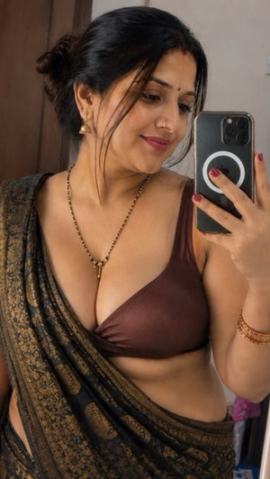 Woman in brown bra and patterned sari taking mirror selfie indoors.