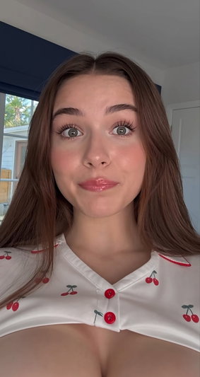 Woman with long brown hair wearing a white cherry-print top, indoors.