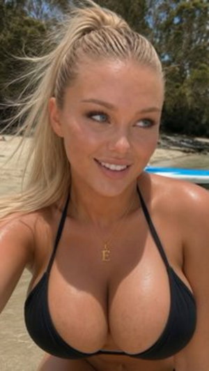 Blonde woman in black bikini top at beach, smiling, hair in high ponytail.