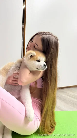 Woman with long hair in pink outfit holding a puppy on green mat indoors.
