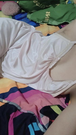 Woman in white slip lying on colorful bed.