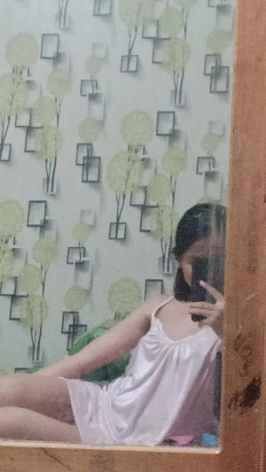 Woman in white slip dress taking mirror selfie indoors.
