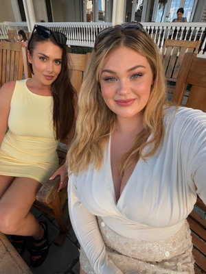 Two women in dresses posing for a selfie outdoors on a patio.