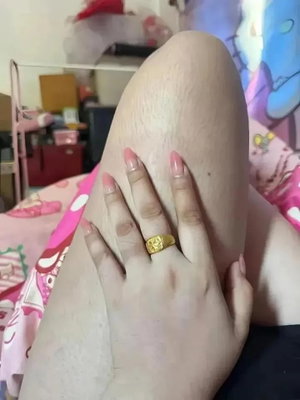 Woman's hand with gold ring resting on thigh in bedroom.