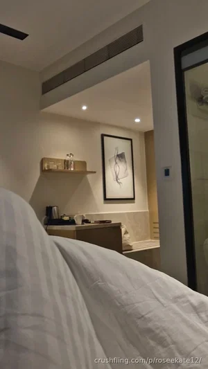 Bedroom interior with striped bedding, small desk, framed art, and bathroom visible in background.