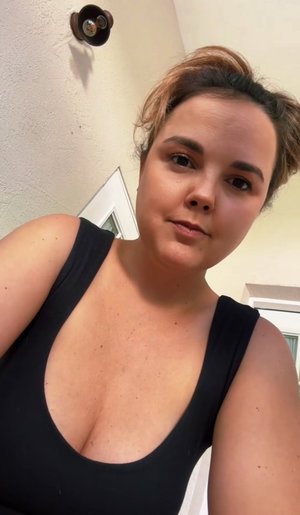 Woman in black tank top with hair up, indoors, looking at camera.