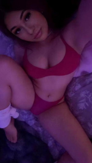 Woman in red lingerie lying on bed taking selfie.