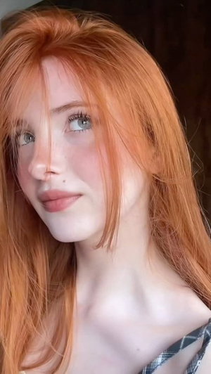 Woman with red hair and green eyes wearing a plaid top, indoors.