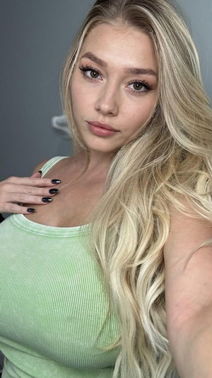 Blonde woman in green tank top taking selfie indoors.