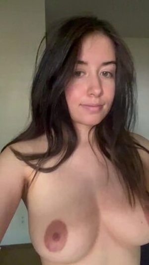 Woman with long dark hair posing topless indoors.