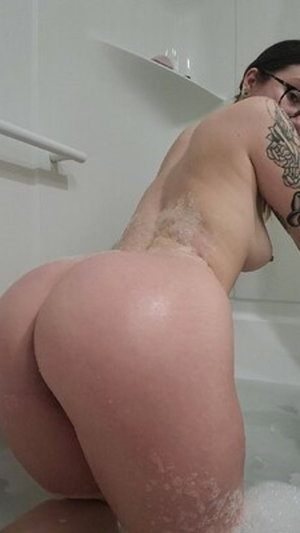Woman with glasses and tattoo in bubbly bathtub.