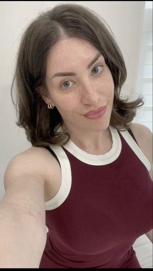 Woman with brown hair in a maroon tank top taking a selfie indoors.