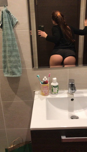 Curvy woman in black top and shorts taking mirror selfie in bathroom.