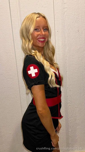 Woman with blonde hair in a black and red nurse-themed dress posing indoors.