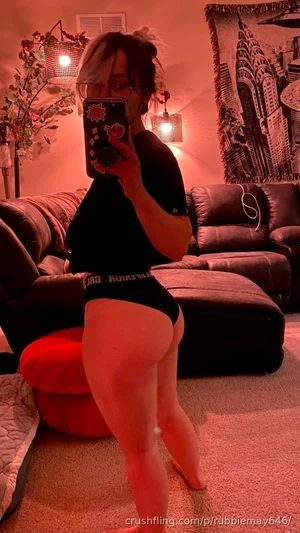 Woman in black top and underwear poses in living room with red lighting.