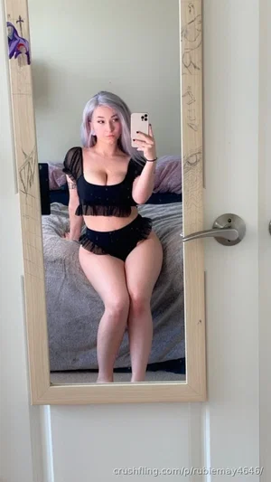 Woman with silver hair in black lingerie takes mirror selfie in bedroom.