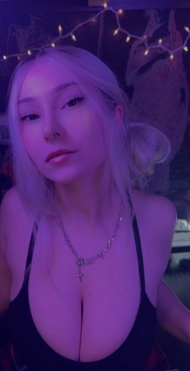 Blonde woman in black top with necklace, purple lighting, string lights in background.
